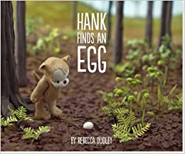photograph of a small plush bear in a forest looking at an egg. Text reads Hank Finds an Egg