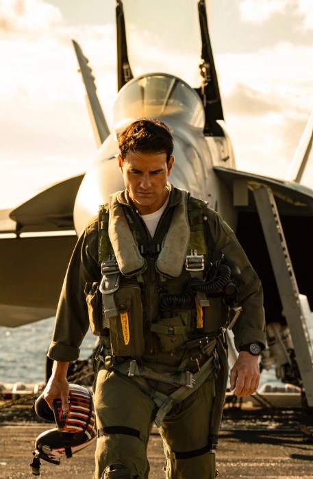 Tom Cruise Wearing Military Uniform Carrying Helmet Walks Away from Fighter Jet in Background