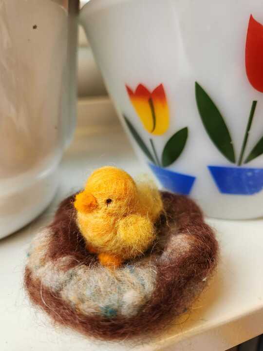 Bird in nest made of needle felting wool. Sitting on window sill.