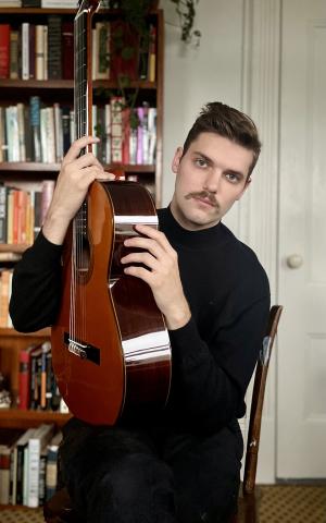 Tim Scott holding his guitar in a room with bookcases behind him