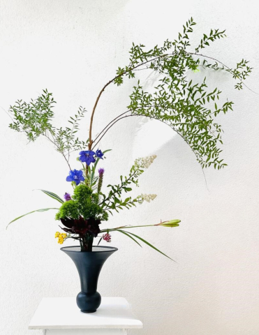 japanese flower arrangement black vase with flowers and greenery against a white wall